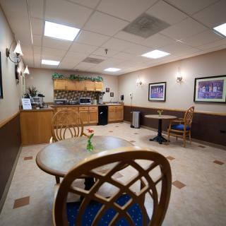 A cozy waiting room with tables and chairs, lit by ceiling lights and adorned with artwork on the walls.