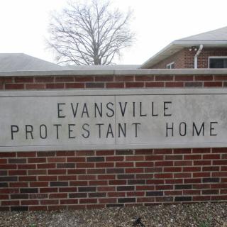 A sign on a brick wall reads 'Evansville Protestant Home' with a building in the background.