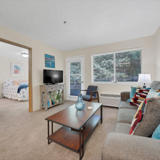 A cozy living room featuring a sofa, coffee table, and TV, with large windows providing natural light.