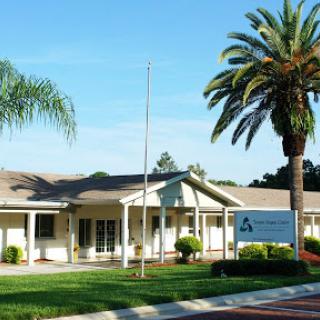 A well-maintained office building surrounded by greenery and palm trees under a clear blue sky.