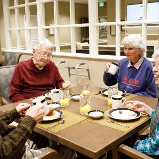 A group of elderly friends enjoying a meal and conversation indoors.