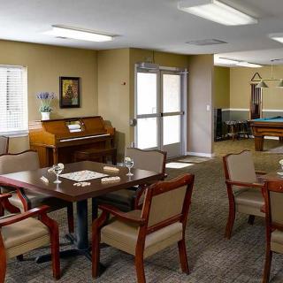 A comfortable community room with tables, chairs, and a piano under bright lighting.