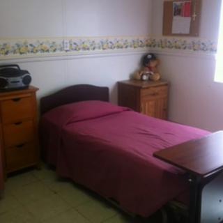 A small bedroom with a single bed covered in a pink bedspread and simple furniture.