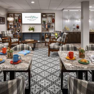 A stylish and comfortable meeting room with patterned carpet, tables set with colorful mugs, and upholstered chairs facing a projector screen.