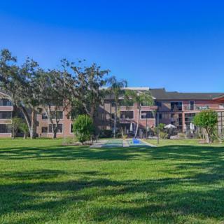 A view of an apartment building with a large grassy area and trees under a clear blue sky.