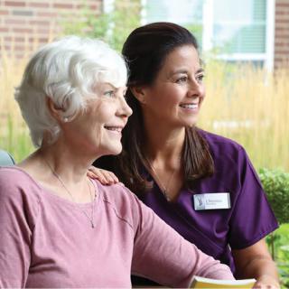 A healthcare worker sitting with an elderly woman outdoors.