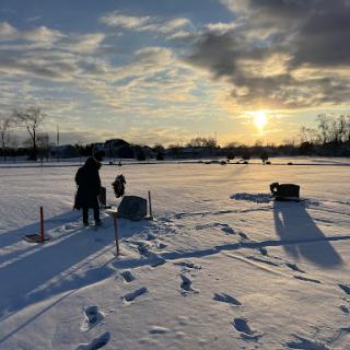 A serene winter landscape at sunset, with a person preparing for ice fishing.
