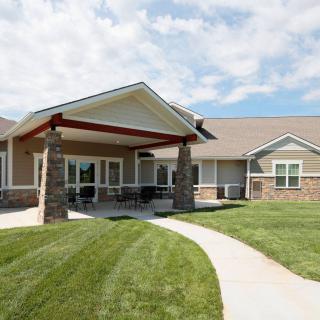 A view of a residential building with a neatly maintained lawn and a walkway, set against a cloudy sky.