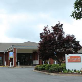 The entrance to a brick building with a landscaped area and signage under a cloudy sky.