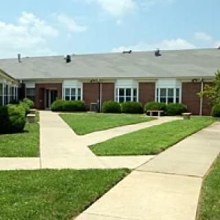 A brick school building with neatly trimmed hedges and a paved pathway under a clear sky.