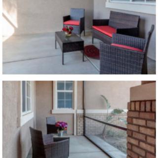 A cozy outdoor patio featuring wicker furniture with red cushions and a small table adorned with flowers.