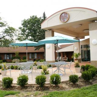 A building entrance with outdoor seating and umbrellas on a landscaped patio.
