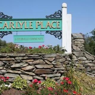 Entrance sign for Carlyle Place surrounded by a stone wall and colorful flowers.