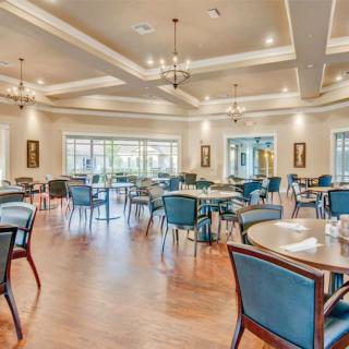 A spacious dining area with arranged tables and chairs, featuring ceiling lights and large windows.