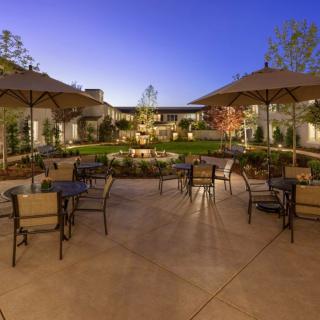 A beautifully landscaped garden patio in the evening with tables and chairs arranged under umbrellas.