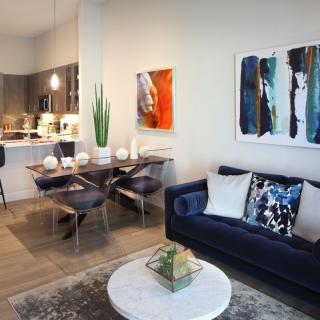 A modern living room with a navy blue sofa, colorful artwork, and an adjacent dining area.