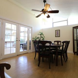A cozy dining area featuring a wooden table with chairs, illuminated by natural light and complemented by a ceiling fan.
