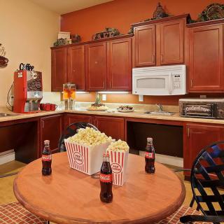 A cozy kitchen with a round table featuring popcorn and soda, surrounded by wooden cabinets and appliances.