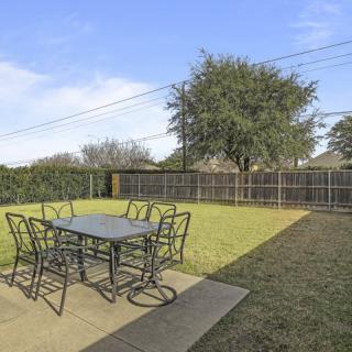 A backyard patio with a table and chairs overlooking a lawn surrounded by a fence.