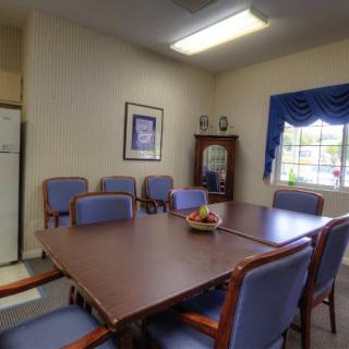 A small meeting room featuring a conference table surrounded by chairs, with a window and decorative elements.