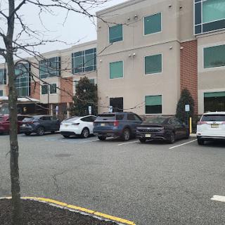 A view of a commercial building with a parking lot filled with cars, surrounded by trees.
