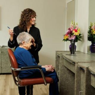 A hairdresser styles an elderly woman's hair at a salon, with a bouquet of flowers on the countertop.