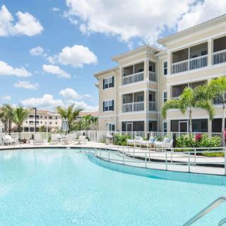 A scenic view of a residential apartment complex with a swimming pool and palm trees under a clear blue sky.