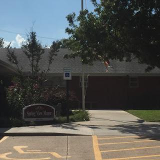 A view of a building with a sign in the foreground and trees nearby.