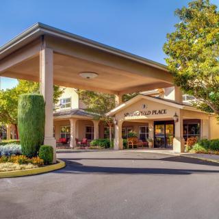 The exterior entrance of a hotel, featuring a covered driveway and landscaped greenery.