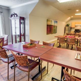 A spacious dining area with multiple tables and chairs, featuring wall artwork and a kitchenette in the background.