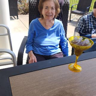 An elderly woman enjoying a drink outdoors on a sunny day.