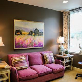 A cozy living room featuring a vibrant purple sofa and a landscape painting.