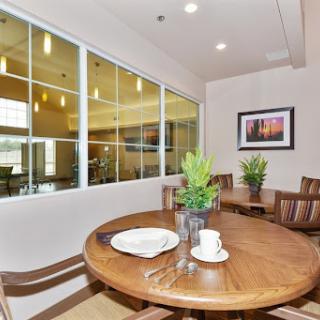 A cozy dining area featuring a wooden table, plants, and large windows allowing natural light.