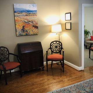 A cozy living room corner with two chairs, a lamp, and a colorful painting on the wall.