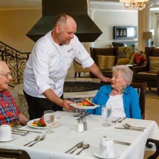 A chef serves a meal to elderly diners at a restaurant.