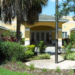 A sunny view of a building entrance surrounded by lush greenery and palm trees.