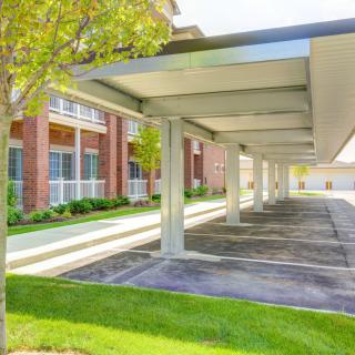 Covered parking area outside an apartment complex with trees and green landscaping.
