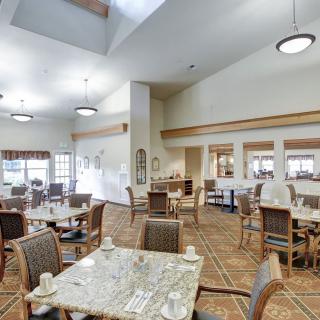 A spacious and well-lit dining area featuring multiple tables and chairs, with a carpeted floor and modern interior design.