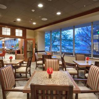 A cozy dining area with neatly arranged tables and chairs, illuminated by ceiling lights and large windows.
