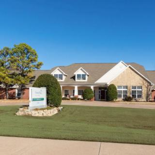 A suburban house with a well-maintained lawn and a sign in the front yard under a clear blue sky.