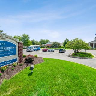 A view of an office complex with a sign, parking lot, and surrounding greenery on a clear day.