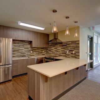 A modern kitchen with wood cabinets, stainless steel appliances, and an island counter with pendant lights.