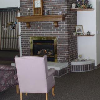 A cozy living room features a brick fireplace, an armchair, and shelves with decor.