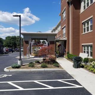 A view of a modern building with a landscaped entrance and parking lot under a clear blue sky.