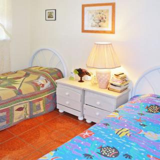 A cozy bedroom featuring twin beds with colorful bedding and a shared nightstand with a lamp.