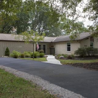 A suburban house with a long driveway surrounded by trees and landscaped greenery.