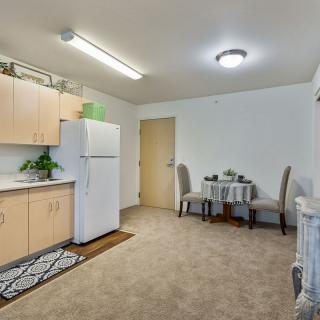 A cozy apartment kitchen with a small dining area, featuring carpet flooring and simple decor.