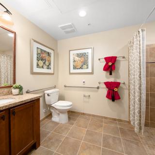 A modern bathroom with neutral tones, featuring a toilet, shower area, and red towels for decoration.