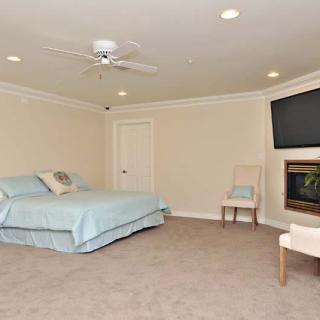 A spacious and minimalist bedroom with a bed, wall-mounted television, ceiling fan, and chair.