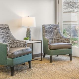 A cozy seating area with two patterned chairs, a small table, and a lamp by the window.